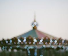 blurry photograph of an amusement park carousel with lights on it's roof and people standing in the background