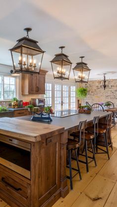 a large kitchen with wooden floors and lots of lights hanging from the ceiling over the island