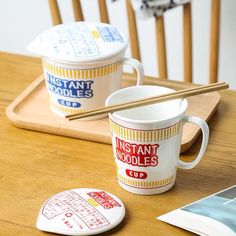 two coffee cups sitting on top of a wooden table next to some chopsticks