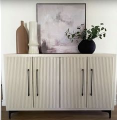 a white cabinet with two vases and a painting on the wall in front of it