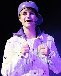 a young man wearing a white jacket and purple hat holding a pair of scissors in his mouth