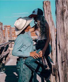 two women in cowboy hats leaning against wooden posts