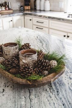 some pine cones are sitting on a wooden tray in the middle of a kitchen counter