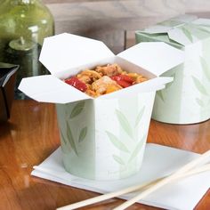 there are two boxes on the table with chopsticks next to it and one has food in it