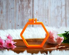 an orange hexagonal object sitting on top of a wooden table next to flowers