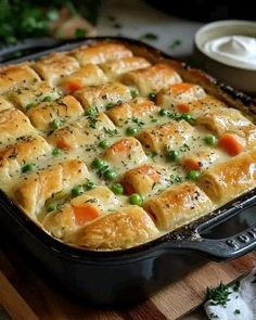 a casserole dish with peas, carrots and chicken in it on a wooden cutting board