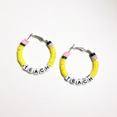 a pair of yellow and pink hoop earrings with the word teach written on each side