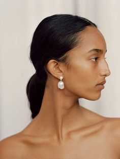 a woman wearing large white earrings with pearls on her ear, looking off to the side