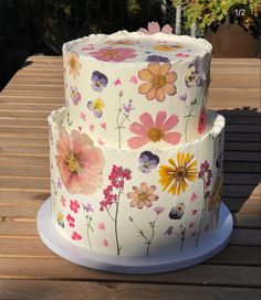 two tiered cake decorated with colorful flowers on a wooden table outside in the sun