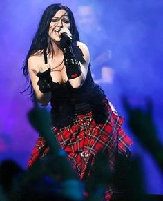 a woman with long black hair wearing a plaid skirt and holding a microphone in her hand