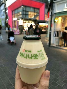 a hand holding up a small bottle of yogurt in front of a store