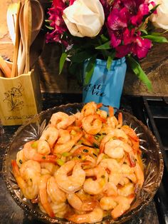 a plate full of shrimp sitting on top of a counter next to a vase with flowers