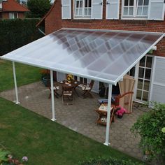 a patio covered with a white plastic roof and table set up on the ground in front of a brick building