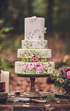 a wedding cake sitting on top of a wooden table in the woods next to flowers