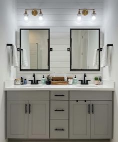 a bathroom with two sinks, mirrors and lights on the wall above them is shown