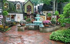 a fountain in the middle of a courtyard surrounded by trees and flowers on a rainy day