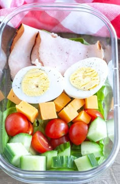 a salad in a plastic container with hard boiled eggs, tomatoes, cucumbers and lettuce