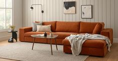 a living room with an orange couch and coffee table in front of a window on the wall