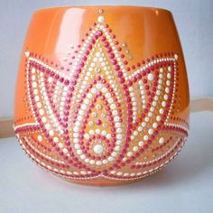 an orange vase with white and pink designs on it's sides, sitting on a table