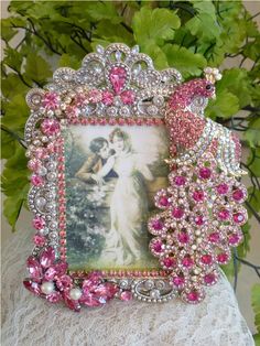 a pink and white photo frame sitting on top of a lace covered table