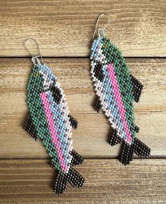 two fish shaped beaded earrings sitting on top of a wooden table