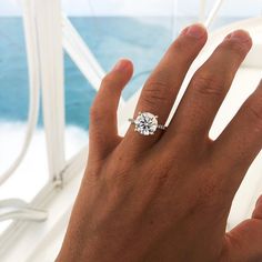 a person's hand with a diamond ring on top of their finger and the ocean in the background