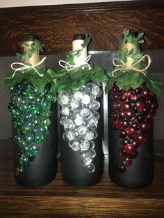 three wine bottles are decorated with grapes and green leaves on the top one is filled with glass beads