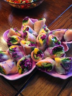 several different types of food are on pink plates next to a bowl of salads