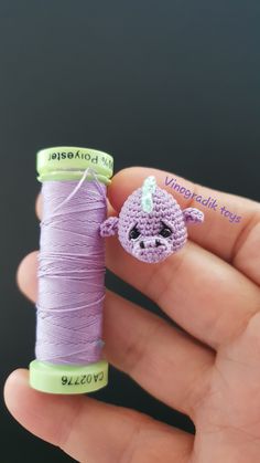 a hand holding a spool of thread with a small crocheted animal on it