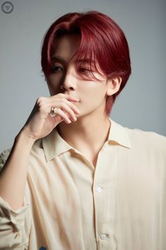 a man with red hair wearing a white shirt and looking off to the side while holding his hand on his chin