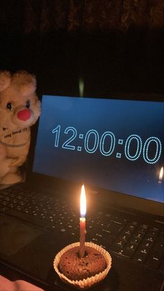 a teddy bear sitting in front of a laptop with a birthday cake on it and a lit candle