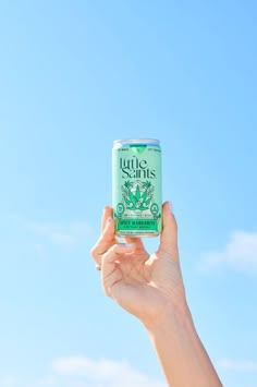 a hand holding up a can of tea against a blue sky