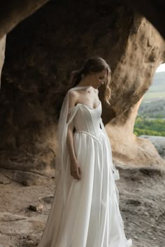 a woman in a white wedding dress standing on rocks with her veil draped over her shoulder