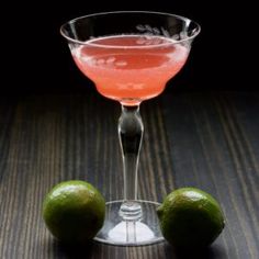 two limes sit next to a margarita glass on a wooden table with a black background