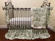 a baby crib with green and white bedding on it's side, next to a wooden floor