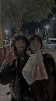 two young people standing next to each other holding bags and giving the peace sign with their fingers