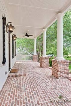 a porch with brick pillars and ceiling fan on the side walk between two white columns