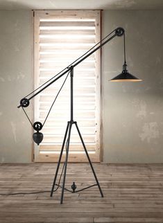 a tripod lamp sitting on top of a wooden floor in front of a window