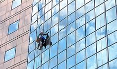 a man hanging from the side of a high rise building while working on glass windows