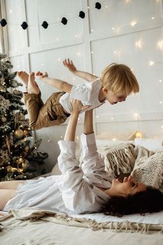 a mother and son playing on the bed in front of a christmas tree with lights