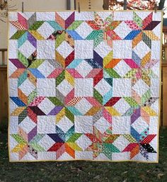 a multicolored quilt hanging from a clothes line in front of a tree and fence