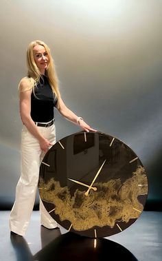 a woman standing next to a large clock on top of a black table with gold trim