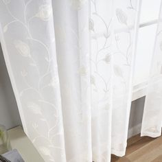 a white curtain with flowers on it next to a window sill and potted plant