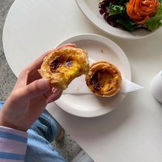 a person is holding a pastry in front of a plate with salad on the side