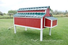 a red and white chicken coop sitting on top of a lush green grass covered field