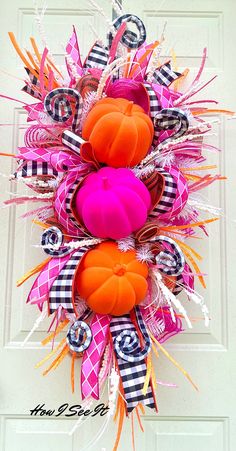 a pink and orange wreath with pumpkins on the front door for halloween time decoration