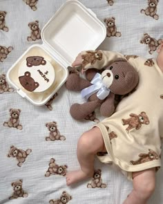 a baby laying in bed next to a brown teddy bear