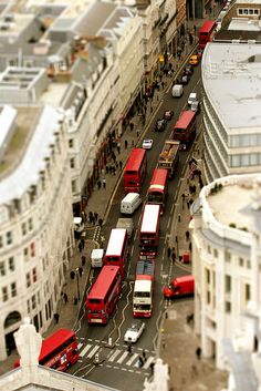 a city street filled with lots of red double decker buses next to tall white buildings