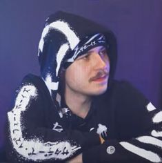 a man wearing a black and white hoodie sitting at a table with his arms crossed