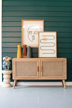 a wooden cabinet sitting in front of a green wall next to vases and pictures